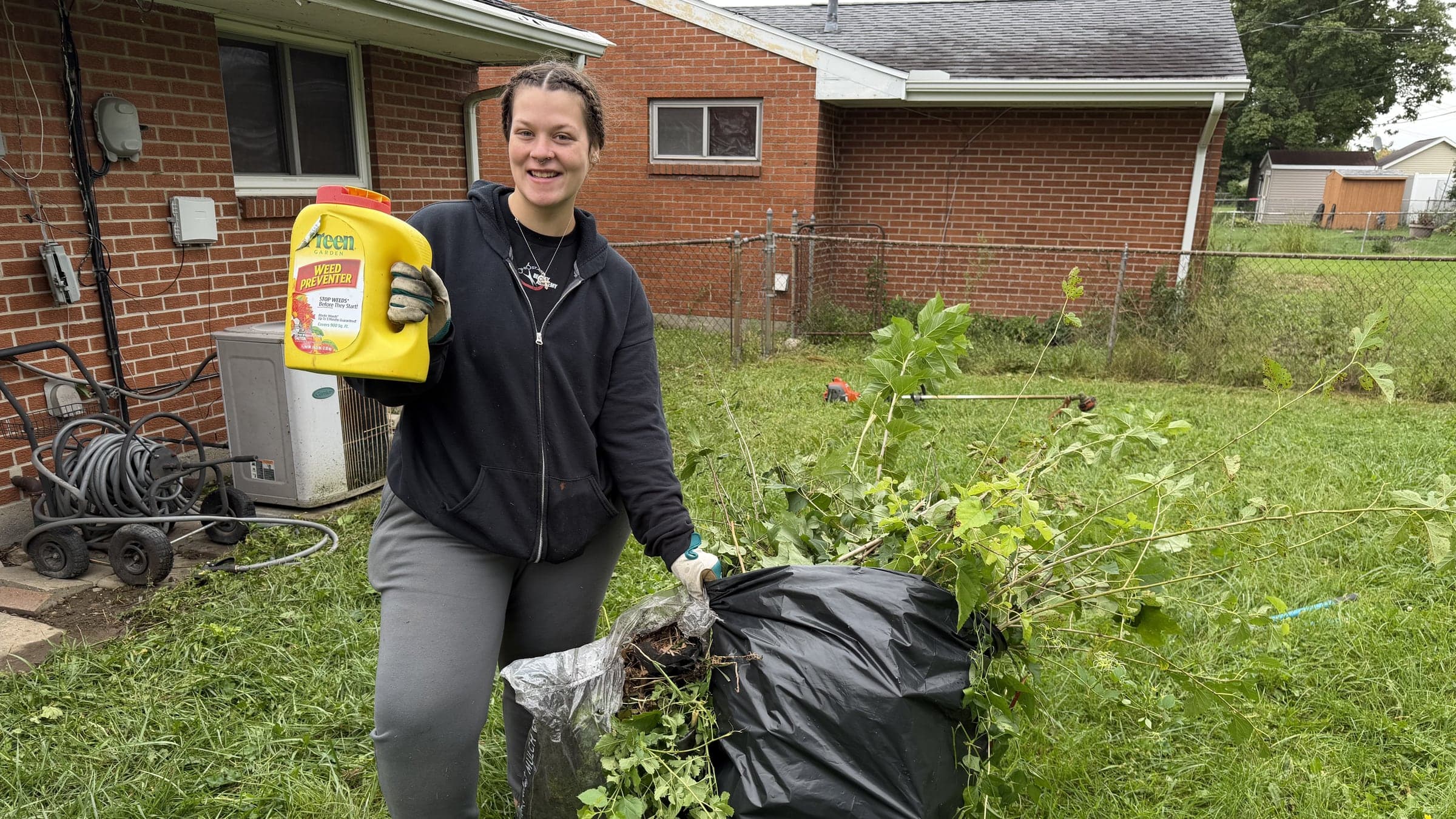 Lawn & Beyond team member smiling next to bags of cleared yard debris after a cleanup