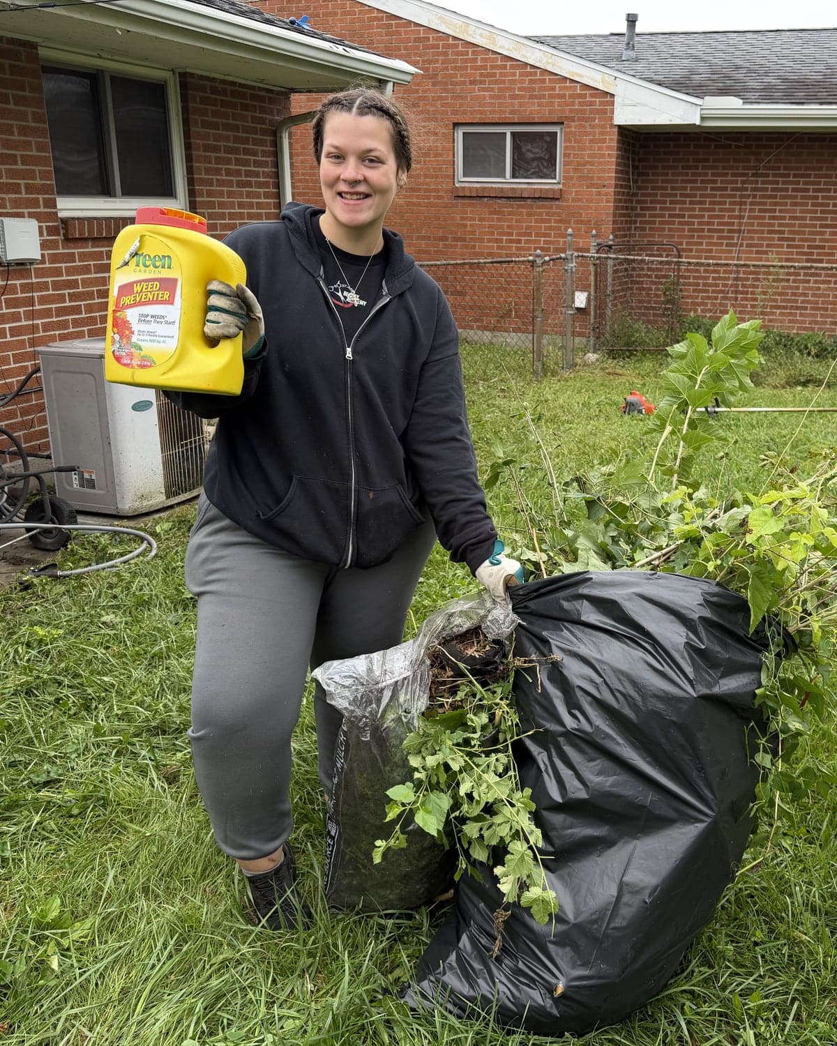 Lawn & Beyond team member smiling with Preen weed preventer and bags of cleared yard debris